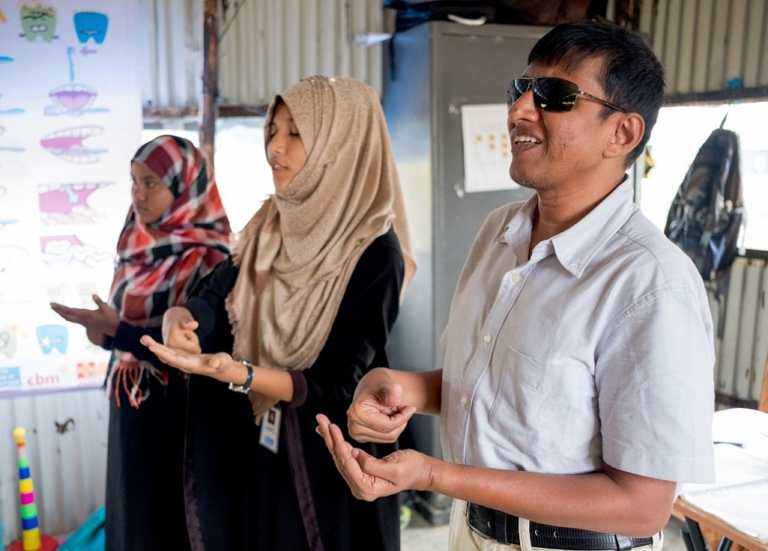 Two women wearing hjiab and a man wearing sunglasses demonstrate hand signs