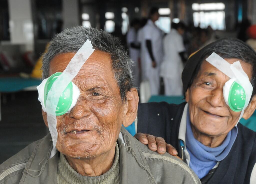 Two men wearing surgical eye patches smile at the camera.