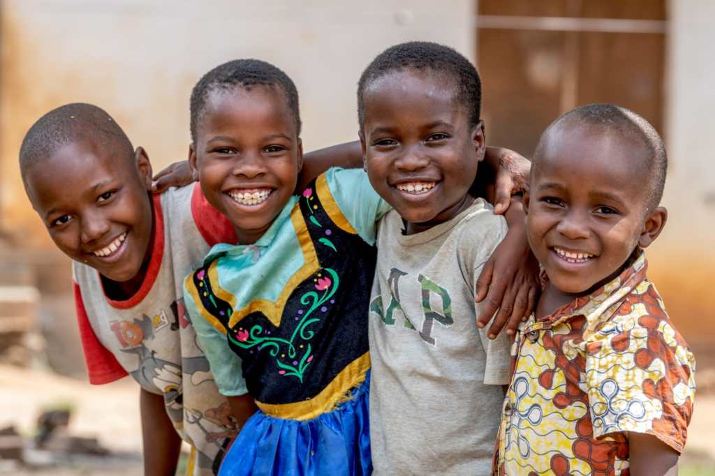 Ramadhan (10) smiling alongside his brothers Ramadhani and Jumaa, and neighbour Mariam, with their arms around each other