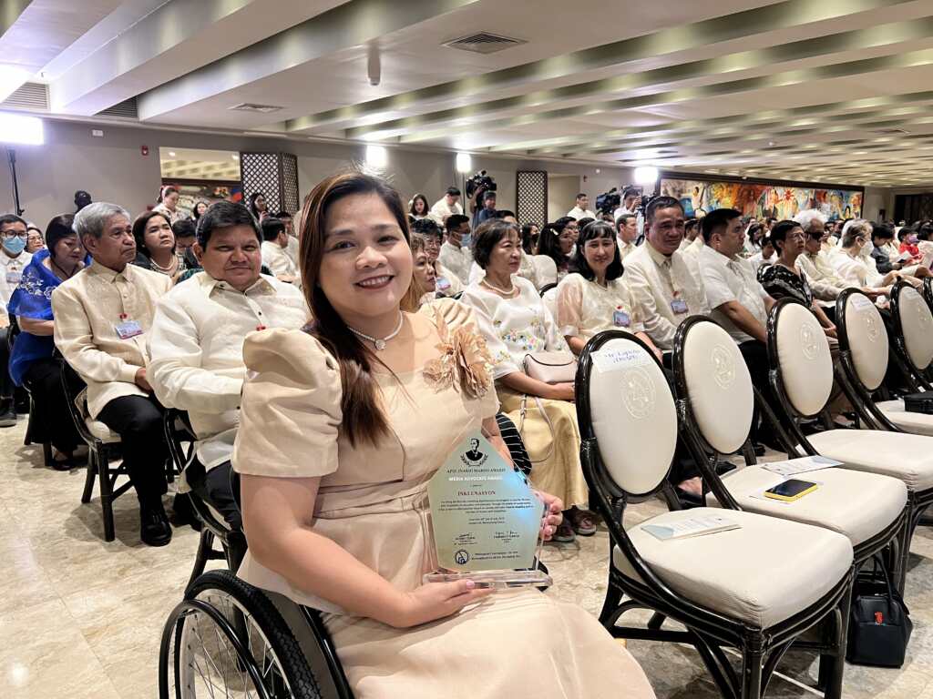 Jennifer Garcia, in a wheelchair, holding the plaque of recognition on behalf of the Inklunasyon team.