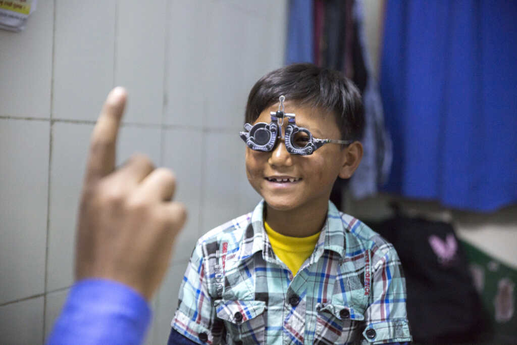 A young boy from Nepal smiles as his eyes are checked.