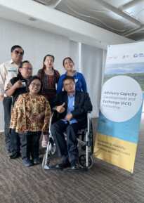 Six persons posing next to the ACE fellowship banner; Three women and three men, of which one man on the right is in a wheelchair. 